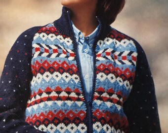 May include: A navy blue zip-up cardigan featuring a geometric pattern in red, white, and light blue. The cardigan has a high collar and is worn over a light blue shirt. The sleeves are navy blue with small white dots.