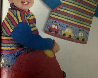 May include: A long-sleeved knit jumper featuring horizontal stripes in yellow, red, green, and blue. The lower section includes a light blue band with a graphic of three cars and the text BEEP! BEEP! BEEP! The jumper has solid blue sleeves.