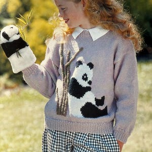 Könnte beinhalten: Ein helllila Strickpullover mit einem Panda-Bären-Design in Schwarz und Weiß. Der Pullover wird mit einem passenden Panda-Bären-Fäustling und einer schwarz-weiß karierten Hose kombiniert. Ein schwarz-weiß gestreiftes Stirnband vervollständigt das Outfit.