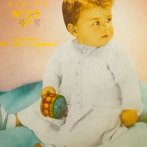May include: A vintage image of a baby wearing a white cardigan and matching outfit, holding a colorful toy. The image has text that reads "Sirdar Sunshine Series No. 29". The baby is sitting on a blue and pink surface.
