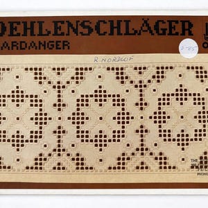 May include: A vintage textile sample featuring a detailed Hardanger embroidery design. The sample is on a light beige background with a repeating pattern of geometric shapes in a darker beige color. The top of the sample has the text "OEHLENSCHLÄGER HARDANGER".