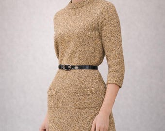 May include: A gold-coloured knitted dress with a high neckline and three-quarter sleeves. The dress has a black belt at the waist and two front pockets. The model is wearing a ring.