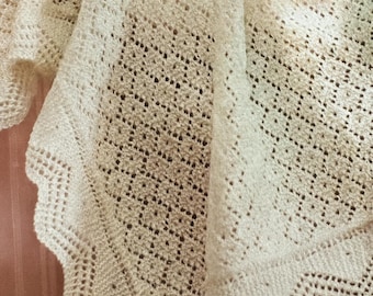 Puede incluir: Chal de color crema, tejido abierto con borde festoneado. El chal está hecho de un hilo suave y texturizado, y presenta un delicado patrón de encaje. El diseño tiene forma de triángulo.