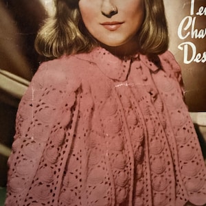 Könnte beinhalten: Vintage-Bild einer Frau, die einen rosa, offen gewebten Umhang mit einem gewellten Design trägt. Der Umhang hat einen runden Kragen und einen Knopfverschluss. Die Frau hat helle Haut, blondes Haar und blickt den Betrachter an. Der Hintergrund ist braun.