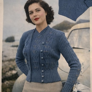 Może przedstawiać: Niebieski kardigan w stylu vintage i pasujący sweter z okrągłym dekoltem. Kardigan ma zapinany na guziki przód i ozdobne szwy. Kobieta na zdjęciu ma na sobie beżową spódnicę. Tło obejmuje samochód i scenę nadmorską.