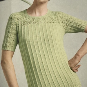 Può includere: Un top in maglia verde chiaro con maniche corte. Il top presenta un design a coste sul corpo e un motivo traforato decorativo sulla parte superiore del petto e sulle maniche. La modella indossa una gonna colorata.