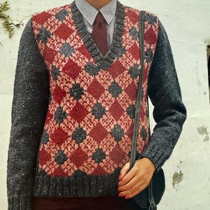 May include: A V-neck sweater with a red and gray diamond pattern over a collared shirt and tie. The sweater has gray sleeves and a black purse is hanging from the shoulder.