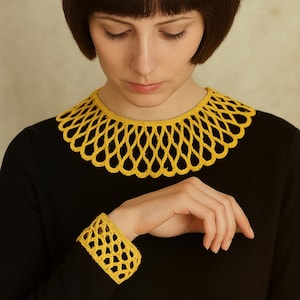 Könnte beinhalten: Schwarzes Kleid mit gelbem Häkelkragen und Manschette. Das Lochmuster des Kragens und der Manschette bildet einen auffälligen Kontrast zum einfarbigen schwarzen Stoff. Die gelbe Farbe sorgt für einen Hauch von Helligkeit.