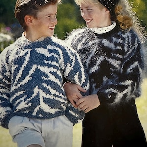 May include: Two children wearing matching knit sweaters with a blue and white zebra stripe pattern. The boy wears khaki shorts, while the girl wears black shorts and a polka dot scarf. The sweaters have a crew neck.