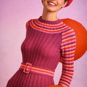 Puede incluir: Una mujer con un vestido de punto acanalado de estilo vintage en tonos morados y rosas, con cinturón a juego y boina roja. El vestido presenta detalles a rayas y se combina con faroles de papel naranja, creando una estética retro.