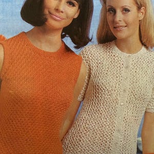 May include: Two women wearing vintage knitted tops. One woman wears an orange sleeveless top, the other a cream-colored button-up cardigan. Both tops have a textured, open-weave design. They are wearing orange skirts and bracelets.