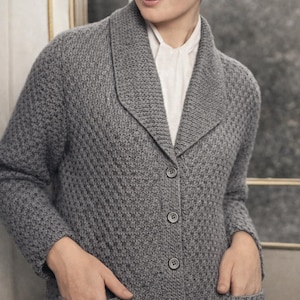 May include: A grey, textured cardigan with a shawl collar and button closure. The cardigan has two front pockets and is worn over a white collared shirt. The fabric appears to be a knitted material.