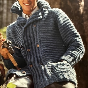 Puede incluir: Un cárdigan azul tejido con cuello chal y botones de madera. El suéter de manga larga tiene una textura acanalada y bolsillos. La persona lleva pantalones negros y sostiene una caña de pescar.