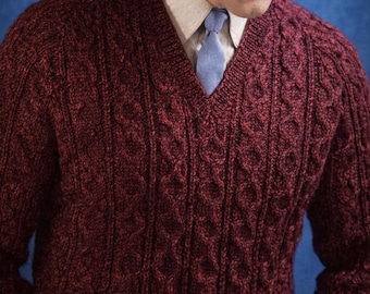 May include: A burgundy V-neck sweater with a cable knit design. The sweater is worn over a light-coloured collared shirt and a blue tie. The background is a solid blue.