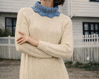 May include: A cream-coloured ribbed knit sweater dress with a blue scalloped collar. The dress is paired with a blue denim skirt and a white headband. The model is standing in front of a white house.