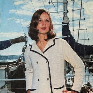 May include: Vintage knitting pattern leaflet titled "Shepherd" with a woman wearing a cream-colored double-breasted jacket with black trim. The leaflet indicates sizes 32-40 inches. The jacket has pockets and gold buttons.