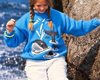 May include: A bright blue long-sleeve knit jumper featuring a graphic design of a black and white whale with a water spout. The jumper has a crew neckline and ribbed cuffs. The whale motif is centred on the front of the garment.