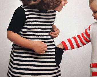 May include: A black and white striped dress with black sleeves and a pocket. Another child's arm is visible, wearing a red and white striped sleeve. The children's clothing has a retro, vintage style.