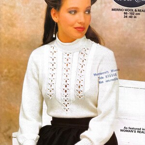 May include: White knitted sweater with a high neck and a delicate lace pattern. The sweater is shown on a model wearing a black skirt. The text "JAEGER Wool. Silk" is visible in the top right corner of the image.