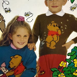 Könnte beinhalten: Zwei Kinder tragen gestrickte Pullover mit Winnie Puuh. Der Pullover des Mädchens ist blau mit Puuh und Ferkel, während der Pullover des Jungen braun ist mit Puuh, der Löwenzahn bläst. Beide Pullover haben einen weißen Hintergrund mit gelben Bienen.
