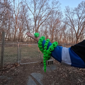 May include: A bright green snake-shaped toy made of plastic. The toy is coiled around a person's arm.