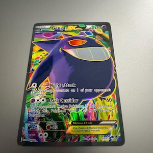 May include: A Gengar EX Pokémon trading card. The card features a large purple Gengar character with a wide grin and orange eyes. The card has a holographic background with text that reads "Night Attack" and "Dark Corridor".