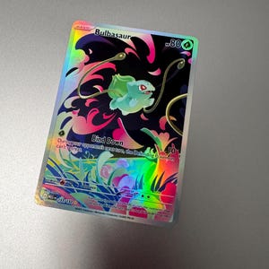 May include: A holographic Bulbasaur trading card. The card features a green Bulbasaur with a black and pink background. The card has the text "Bulbasaur" and "80" along with other game-related text.