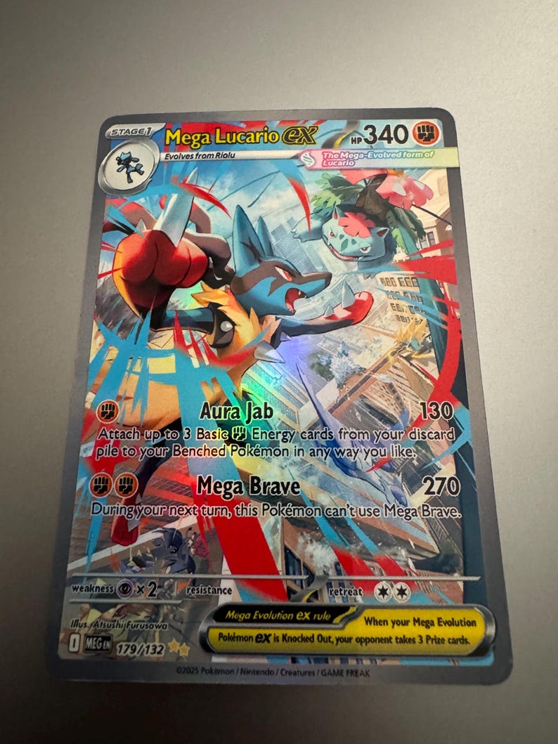 Puede incluir: Una tarjeta coleccionable Pok&eacute;mon Mega Lucario EX hologr&aacute;fica. La tarjeta presenta un personaje Lucario azul y rojo con el texto "Aura Jab" y "Mega Brave". La tarjeta tambi&eacute;n incluye el texto "Mega Evolution EX rule" y "When your Mega Evolution Pok&eacute;mon EX is Knocked Out, your opponent takes 3 Prize cards."