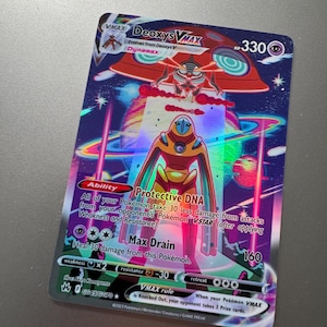 May include: A holographic Deoxys VMAX trading card featuring a colorful space background with planets and a red UFO. The card displays 330 HP, the Protective DNA ability, and the Max Drain attack. Text includes card details and game rules.