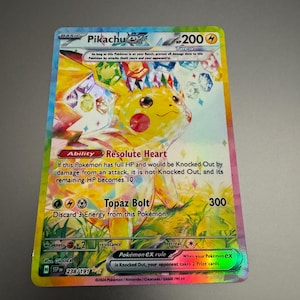 May include: A holographic Pikachu EX Pokémon trading card. The card features a yellow Pikachu with a gem-like design, and the text "Pikachu EX" at the top. The card has a HP of 200 and the ability "Resolute Heart".
