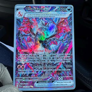 May include: A holographic Charizard ex Pokémon card. The card features a detailed illustration of Charizard with red, purple, and blue accents. The card text includes "Infernal Reign" and "Burning Darkness". The card is a stage 2 evolution.