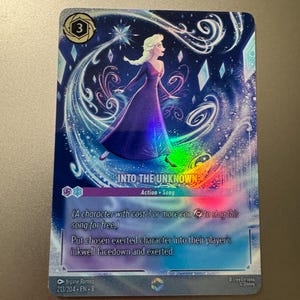May include: A collectible card featuring Elsa from Disney's Frozen, with the text "INTO THE UNKNOWN." The card has a holographic effect with a blue and purple color scheme. The card's design includes a character illustration and game instructions.
