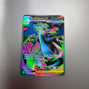 May include: A Mega Charizard X EX Pokémon card. The card features a vibrant illustration of a dragon-like creature with blue, black, and pink accents. The card has the text "Mega Charizard X EX" and "Inferno X" printed on it.