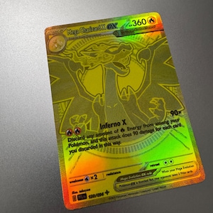 May include: A gold holographic Mega Charizard X EX Pokémon card. The card features a detailed illustration of Charizard and text that includes "Inferno X" and "HP 360". The card has a rainbow holographic effect.