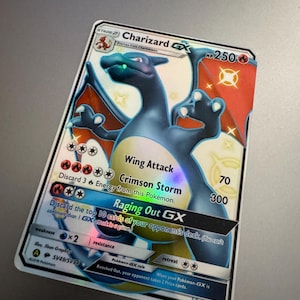 May include: A Charizard GX Pokémon trading card. The card features a blue and orange Charizard illustration with the text "Wing Attack" and "Crimson Storm". The card has a holographic foil finish and the text "HP 250".
