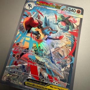 Puede incluir: Una tarjeta coleccionable Pok&eacute;mon Mega Lucario EX hologr&aacute;fica. La tarjeta presenta un personaje Lucario azul y rojo con el texto "Mega Lucario EX", "Aura Jab" y "Mega Brave". La tarjeta tiene 340 HP.
