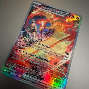 May include: A holographic Pokémon card featuring Team Rocket's Moltres ex. The card has a fiery orange and red design with a character illustration. Text includes "Flame Screen" and "Evil Incineration". The card is a collectible item.