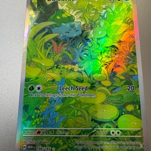 May include: A holographic Bulbasaur Pokémon card. The card features a green Bulbasaur in a lush, green environment. The card text includes "Leech Seed" and "HP 70". The card is part of the 166/165 set.