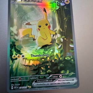 Puede incluir: Una tarjeta coleccionable Pokémon Pikachu EX holográfica. La tarjeta presenta un personaje Pikachu amarillo en un entorno forestal. La tarjeta tiene el texto "Pikachu EX" y "Thunderbolt". La tarjeta está numerada 276/217.