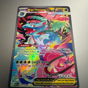 May include: A holographic Mega Venusaur EX Pokémon trading card. The card features a vibrant illustration of the evolved form of Venusaur, with a HP of 380. The card has the text "Jungle Dump" and "Solar Transfer".
