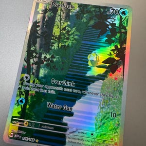 May include: A holographic Psyduck Pokémon trading card. The card features a colorful illustration of Psyduck on a staircase in a forest. Text includes "Psyduck", "Overthink", and "Water Gun". The card has a HP of 70.