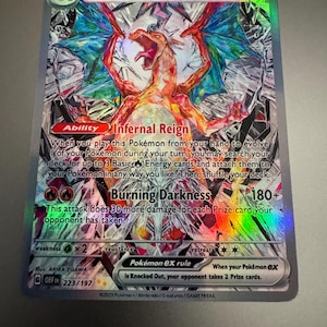 May include: A holographic Charizard ex Pokémon trading card. The card features a fiery orange dragon with blue wings and the text "Charizard ex". The card has the text "Infernal Reign" and "Burning Darkness".