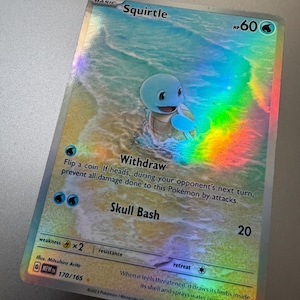 May include: Holographic Squirtle Pokémon trading card. The card features a blue Squirtle character on a beach scene. Text includes "Withdraw", "Skull Bash", and "HP 60". The card has a holographic rainbow effect.