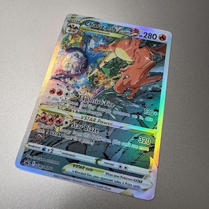 May include: A holographic Charizard VSTAR Pokémon trading card. The card features a vibrant illustration of Charizard in action, with the text "Charizard VSTAR" and "Star Blaze" visible. The card has a HP of 280 and a damage of 320.