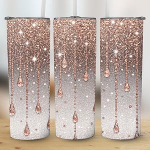 Könnte beinhalten: Drei mit Glitzer bedeckte Becher mit einem Farbverlauf aus Roségold und Silber. Das Design zeigt funkelnde Akzente und hängende Tropfenformen. Jeder Becher hat einen Strohhalm und einen Deckel.