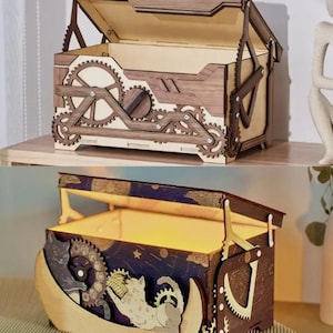 Könnte beinhalten: Zwei Holzkisten mit Klappdeckeln. Die obere Box hat ein Zahnraddesign auf der Vorder- und den Seiten. Die untere Box hat ein Katzen- und Monddesign. Beide Boxen sind aus hellem und dunklem braunem Holz gefertigt.