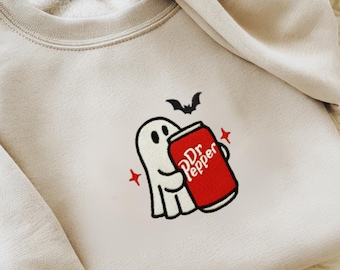 May include: Beige sweatshirt with an embroidered Halloween design. A white ghost holds a red Dr. Pepper can, with a black bat above and red star accents. The sweatshirt has a crew neck and long sleeves.