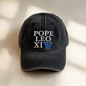 May include: A black, distressed baseball cap with the text "POPE LEO XIV" embroidered in white and blue. The cap has a curved brim and a classic six-panel design, suitable for casual wear.
