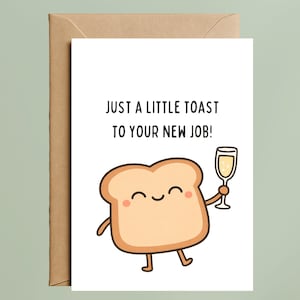 May include: A white greeting card with a brown kraft envelope featuring a cartoon slice of toast with a smiling face, pink cheeks, and thin limbs. The toast holds a champagne flute. The text reads: JUST A LITTLE TOAST TO YOUR NEW JOB!