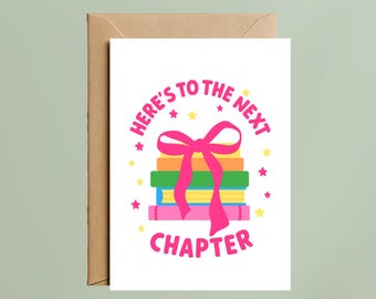 May include: A white greeting card with a stack of four colorful books tied with a bright pink ribbon. The text reads "HERE'S TO THE NEXT CHAPTER" in pink letters, surrounded by small yellow and pink stars. A brown envelope is positioned behind the card.